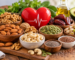 A variety of heart-healthy nuts, dry fruits, and seeds including almonds, walnuts, pistachios, cashews, pumpkin seeds, chia seeds, flaxseeds, and dates arranged around a red heart symbol, representing foods that support healthy cholesterol levels and cardiovascular health.